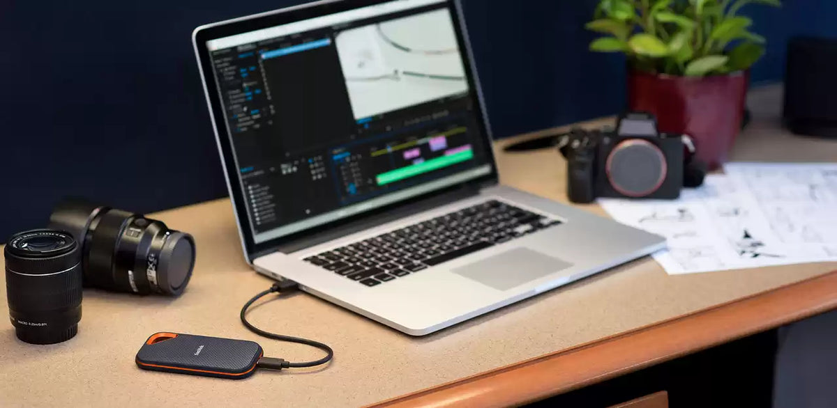 هارد سانديسك Extreme PRO Portable SSD V2 موصول بلابتوب على مكتب بجانب كاميرا وعدسات