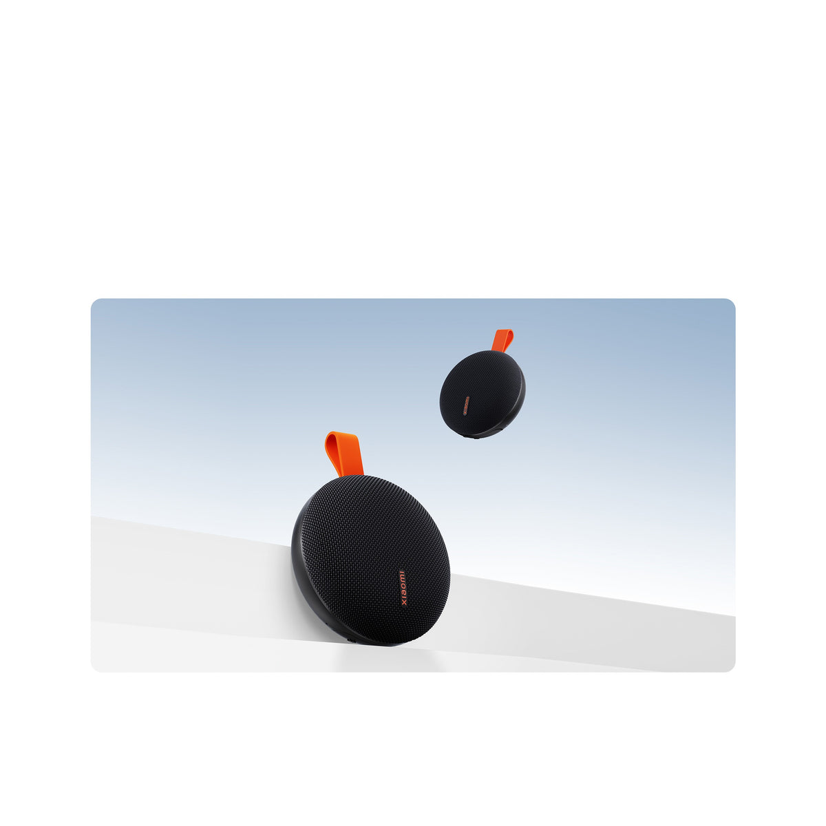 Two Xiaomi Bluetooth Speaker Essential units in black, showing the rounded fabric-covered body and the orange carry strap